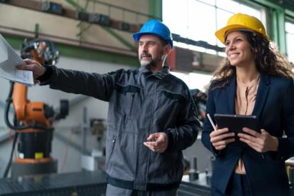 A manufacturing team leader in safety gear observing a process with a frontline operator and guiding them during a gemba walk on the shop floor.