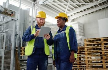 Opérateurs industriels analysant leurs objectifs opérationnels SMART sur un tableau de management visuel digital dans une usine.