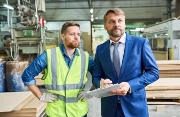 A modern factory floor with an operator and supervisor using digital tools during a Gemba walk or production review.