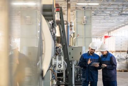 Factory inspector using a digital tablet to complete a quality control checklist on a modern production floor.