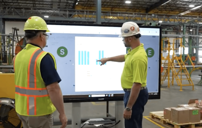A production manager and shop floor operator reviewing real-time production performance data on a digital board in a modern manufacturing facility.