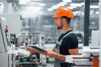 Manufacturing professional using a digital tablet to check production metrics on a clean factory floor, illustrating a modern integrated work system.
