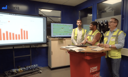Manufacturing executives reviewing real-time production KPIs and cross-site performance metrics on a digital dashboard.